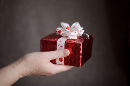 Hands holding gift in package with white ribbon on a dark backgroundの写真素材