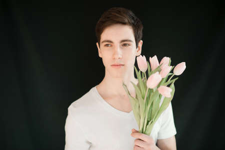 Handsome young man with pink tulips on black backgroundの写真素材
