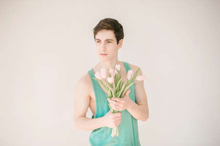 Handsome young man with pink tulips on light backgroundの写真素材