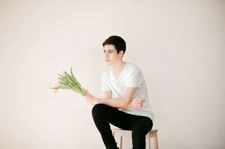Handsome young man with pink tulips on light backgroundの写真素材