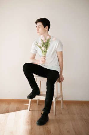 Handsome young man with pink tulips on light backgroundの写真素材