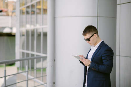 Portrait of a young businessman seeing on his tablet pc on the street. Man in blue suit with dark sunglasses.の写真素材