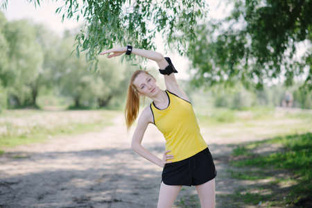 Young fitness woman stretching body before run. Sportsman standing under tree.の写真素材