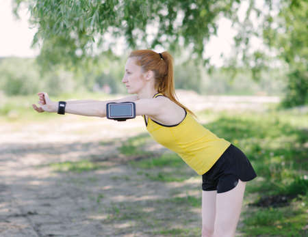 Young fitness woman stretching body before run. Sportsman standing under tree.