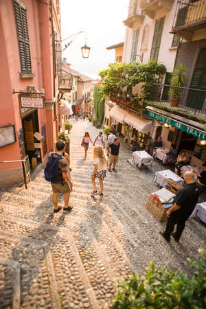 Bellagio. Lake Como. Italy - July 20, 2019: Amazing Old Narrow Street in Bellagio. Lake Como, Italy, Europe. Famous Picturesque Cobblestone Street with Souvenir Shops, Restaurants and Cafes.のeditorial素材