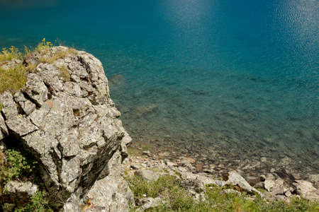 Rock, grass and stones on the shore of a mountain lake in sunny weatherの写真素材