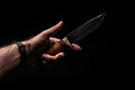 Hunting knife in hand on dark background