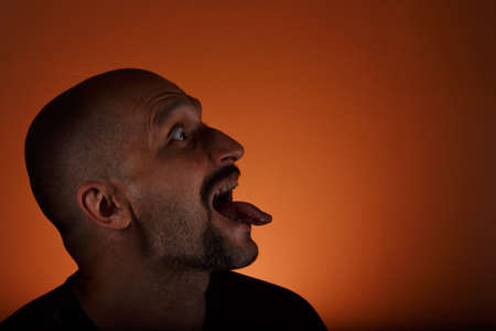 Man with a short haircut, a mustache and a beard shows his tongue in profileの写真素材