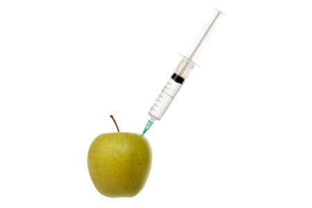 Syringe with colorless liquid stuck into an apple isolated on white.の写真素材