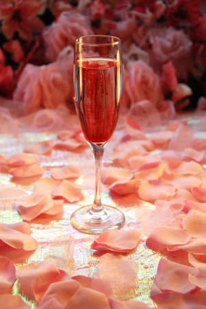 Single glass of pink champagne on a shimmery table surrounded by pink pedals. Background in soft focusの写真素材
