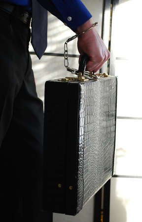 businessman holding a briefcase with handcuffs tied to his handsの写真素材