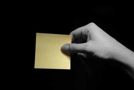 hand holding a blank post-it over black backgroundの写真素材