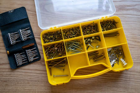 Yellow box with screws and screws on a wooden tabletop. A set of small screwdrivers with interchangeable heads. Top view, close-up.の写真素材