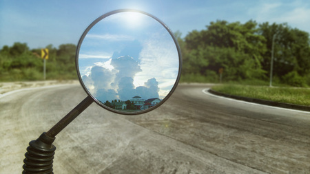 Shot of motorcycle rare view mirror reflecting beautiful sunlight behind white fluffy cloud and road...