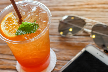 cup of the lemon ice tea with orange and mint on top on the brown bark beautiful texture background with warm light decorated with sunglassesの写真素材