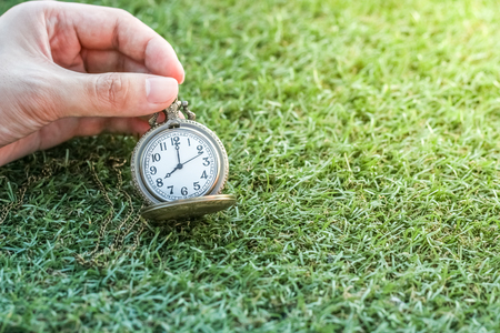 Hand holding vintage pocket gold watch with green grass, abstract for time concept with copy space