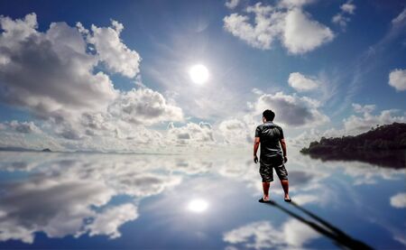 Young man standing in the reflect water of blue sky and sunの写真素材
