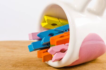 Group colorful pastel of wooden clothespins in coffee cup on wooden board isolated on white backgroundの写真素材