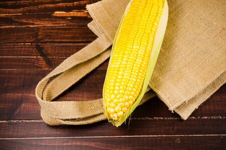 Yellow fresh corn on sack bag on wooden board backgroundの写真素材