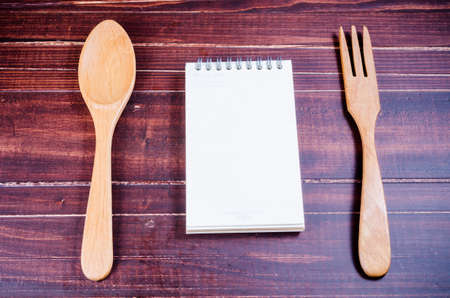 Notebook with wooden spoon and fork isolated on wooden backgroundの写真素材