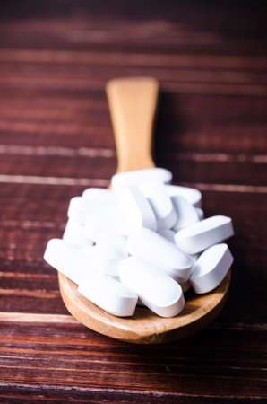 Close up white pills tablets on wooden spoon with wooden board 