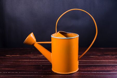 orange garden watering can on wooden board backgroundの写真素材