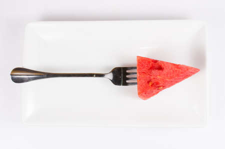 Arange piece of fresh watermelon on dish with fork isolated on white backgroundの写真素材