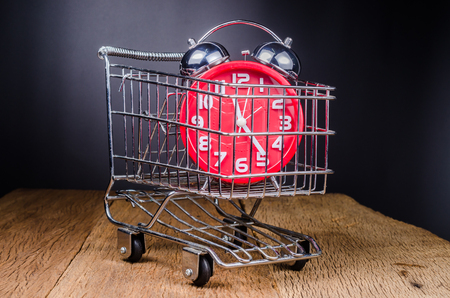 Shopping time concept,Shopping Cart filled with alarm clock on wooden tableの写真素材