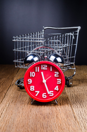 Shopping time concept,Shopping Cart filled with alarm clock on wooden tableの写真素材
