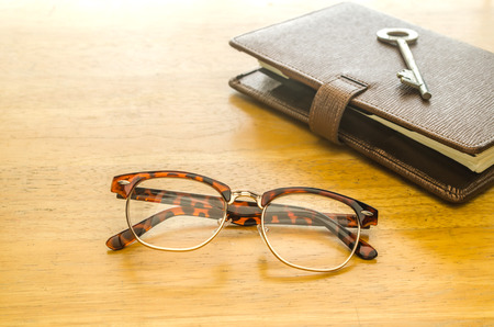 Glasses and brown leather organizer with key on wooden table,key to success, concept imageの写真素材