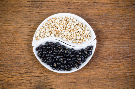 Job's tears and black beans in ying yang porcelain shape on wooden board with wooden board background, agriculture productsの写真素材