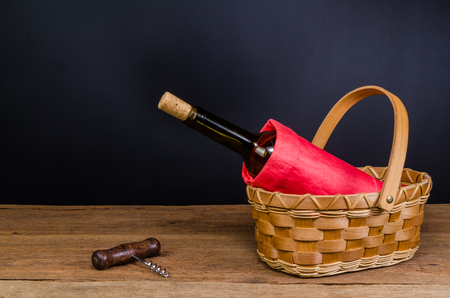 red wine bottles on wicker basket on wooden board and black backgroundの写真素材