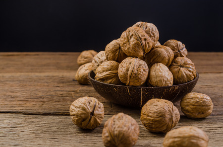 Heap of walnuts in coconut shell on wooden tableの写真素材