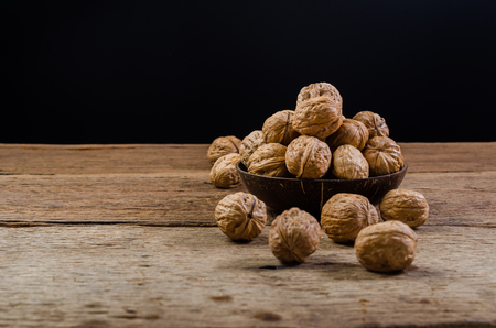 Heap of walnuts in coconut shell on wooden tableの写真素材