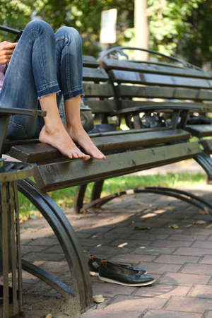 Sitting on the bench with feet. Tired bare feet on wooden settle and shoes under it.の写真素材