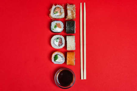 Set of salmon rolls, soy sauce and chopsticks on red backgroundの写真素材