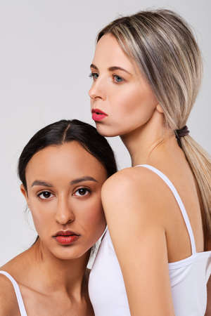 Cute caucasian and african girl models with different types of skin leaning to each otherの写真素材