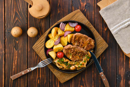 Plate with fried pork fillet, potato wedges, mushrooms and tomatoの写真素材