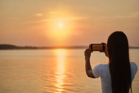 Young woman making photo of sunset with her smartphoneの写真素材