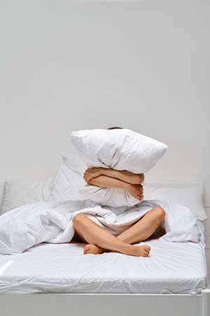 Young woman hugs the pillow and hides her face behind itの写真素材