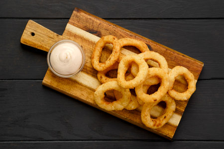 Top view of deep fried breaded squid rings with creamy sauce on wooden serving boardの写真素材
