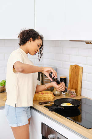 African american woman seasoning scrambled eggs with pepper on a panの写真素材