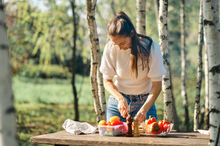Woman makes vegetable salad outdoor at picnic in sunny dayの写真素材