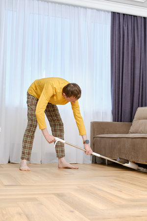 Single middle age man mopping floors under the sofaの写真素材