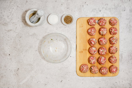 Top view of raw meatballs on wooden cutting board next to empty bowl and spicesの写真素材
