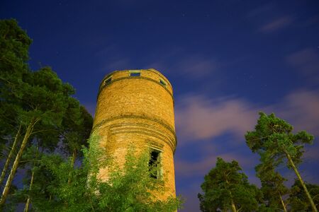 Old brick water tower surrounded with pines at night against the skyのeditorial素材