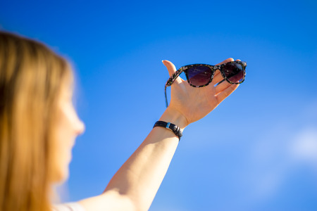 Young woman holding sunglasses against the blue sky at summerの写真素材