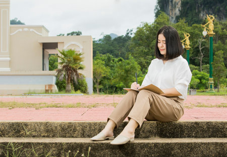 Asian woman sitting in a park on vacation writing a notebookの写真素材