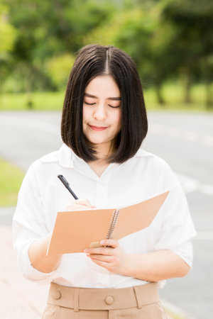 An Asian female student stands and writes in an educational concept notebook.の写真素材