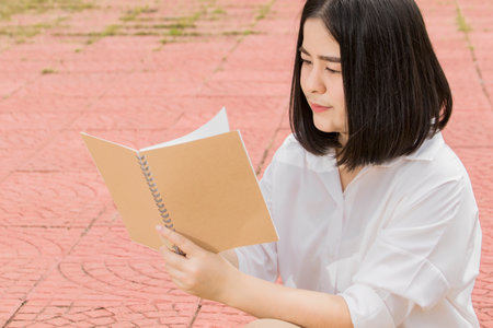 Asian woman sitting and holding a book to read vacation conceptの写真素材